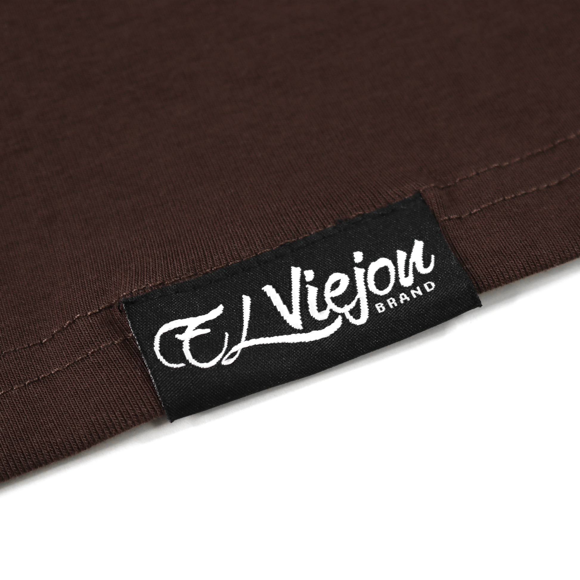 Close-up of a brown polo shirt with a black woven tag featuring the white "El Viejon Brand" logo.