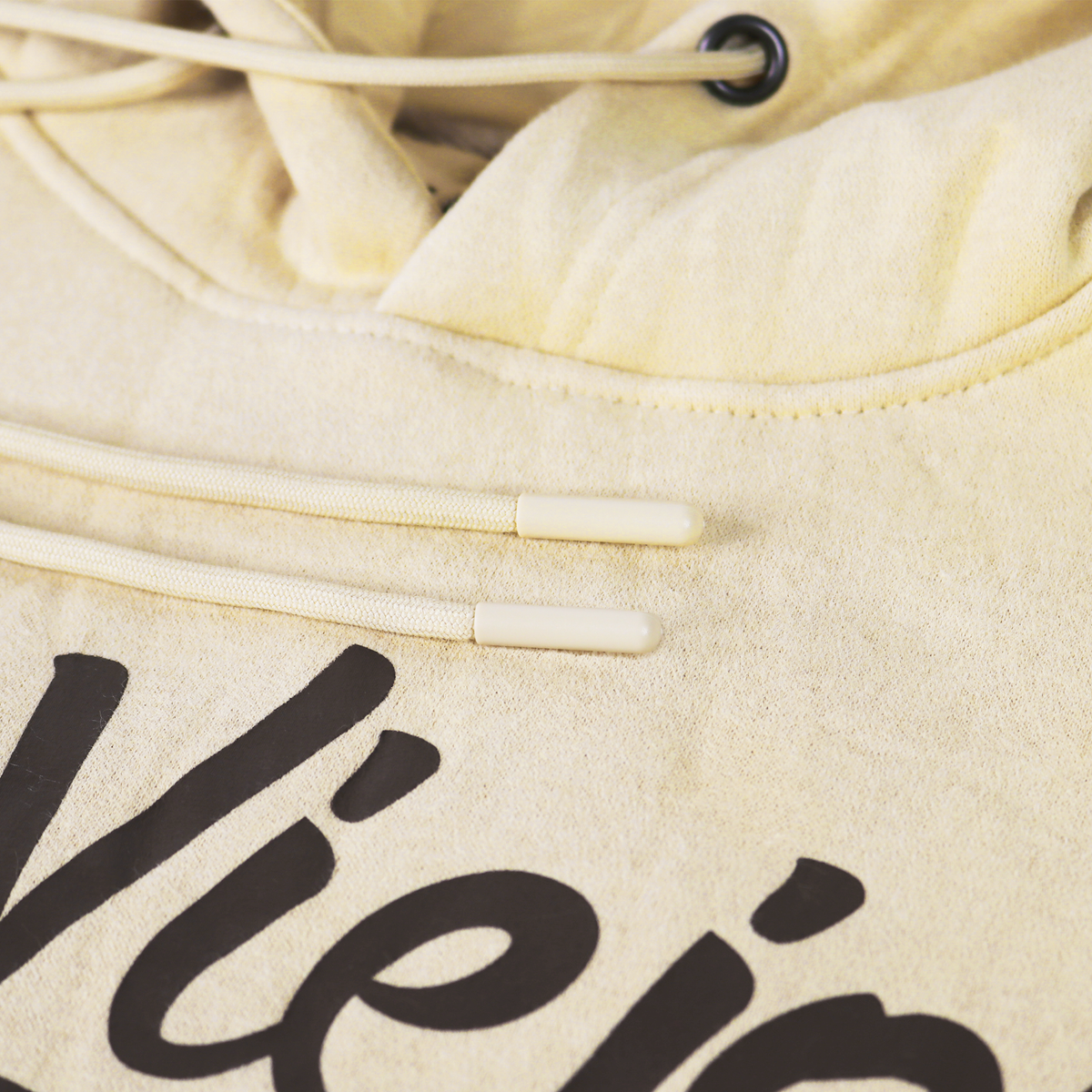 Close-up of a sand-colored cotton/poly fleece hoodie with black screen-printed logo and drawstrings.